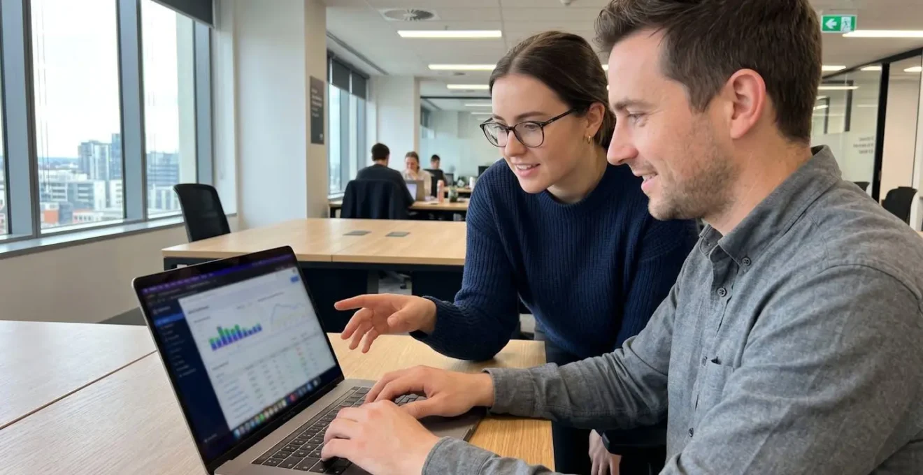 Two marketing professionals leaning over a laptop displaying colourful data charts in a bright modern office